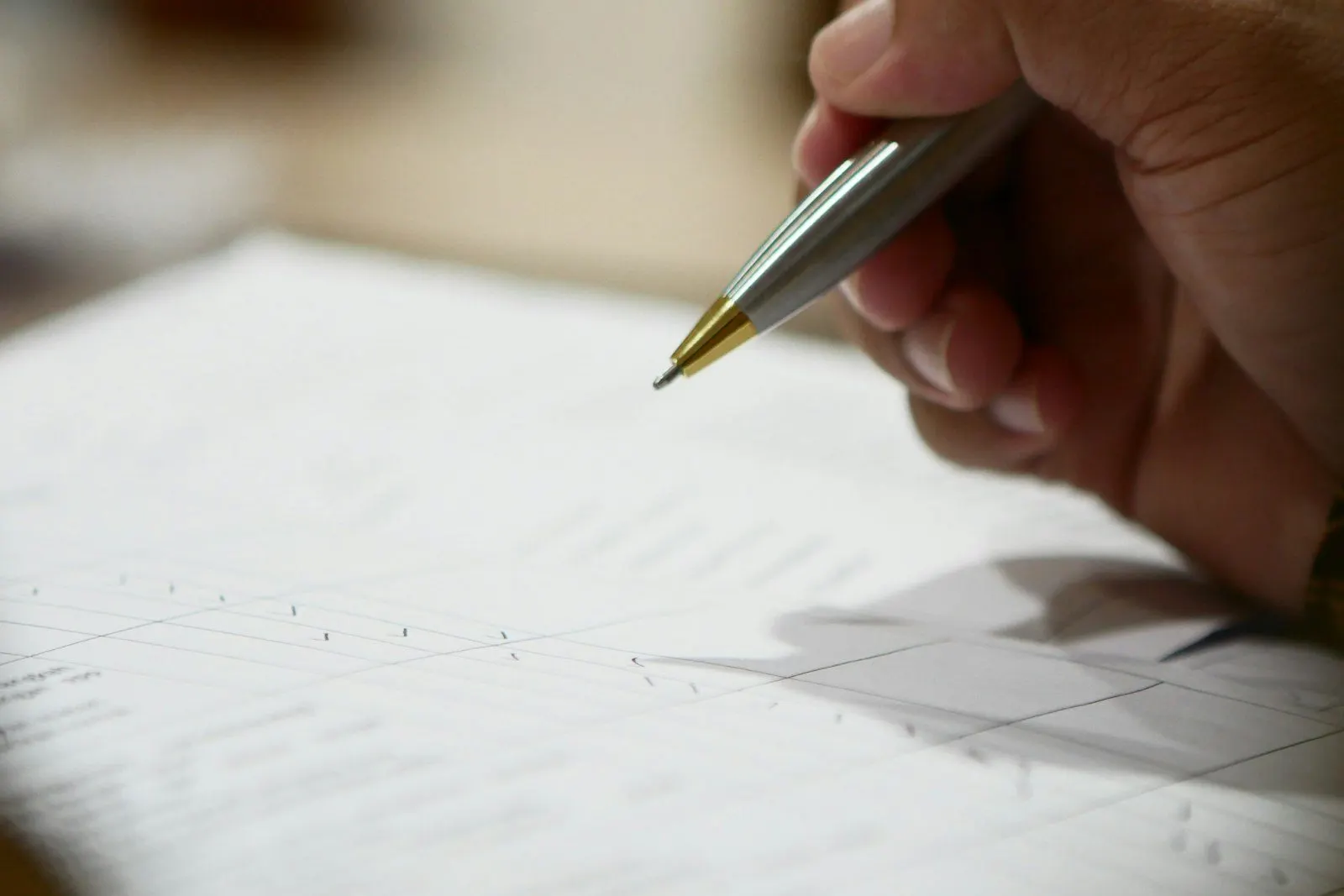 Persona firmando un documento con una pluma sobre el escritorio